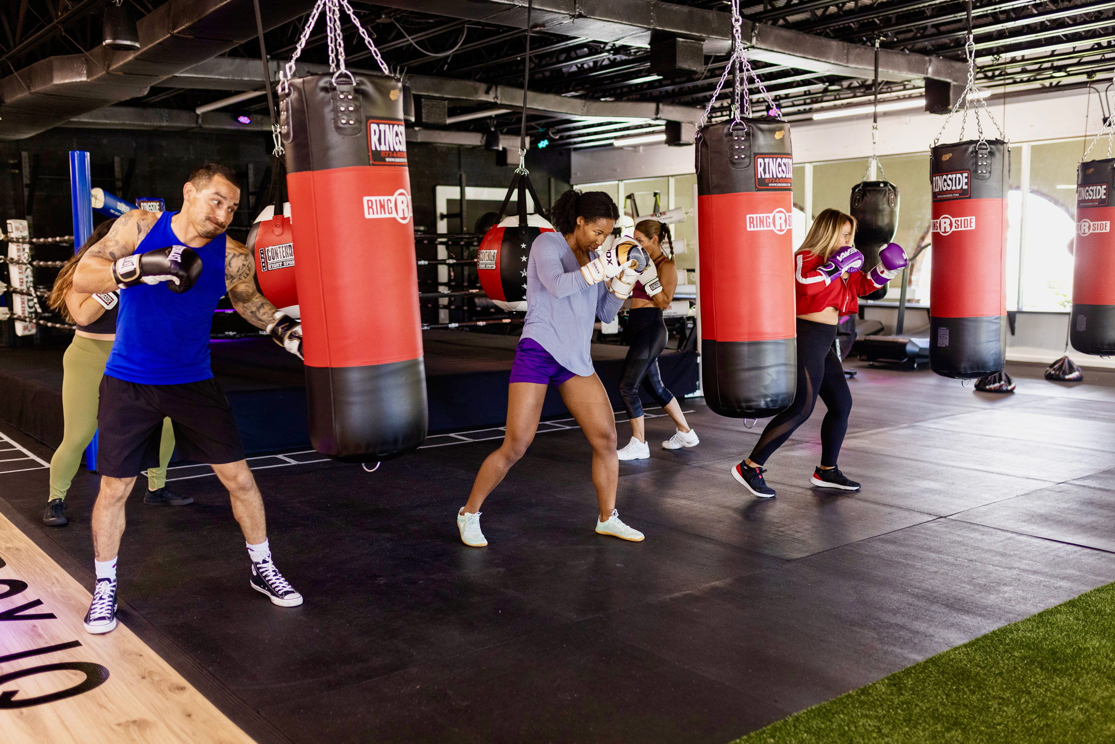 Boxing gym members punching bags in front of a boxing ring